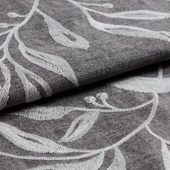 Folded gray curtain fabric with raised white embroidered leaf pattern, overlapping layers; fabric folded to reveal texture and stitch detail in soft, diffuse studio lighting.