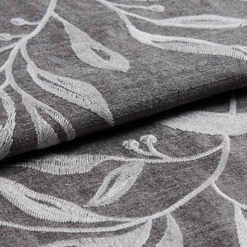 Folded gray curtain fabric with raised white embroidered leaf pattern, overlapping layers; fabric folded to reveal texture and stitch detail in soft, diffuse studio lighting.
