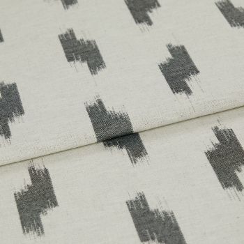 Folded curtain fabric (linen-like) with a central horizontal fold, showing repeating dark gray, brushstroke rectangular motifs on a light beige background in soft, even lighting.