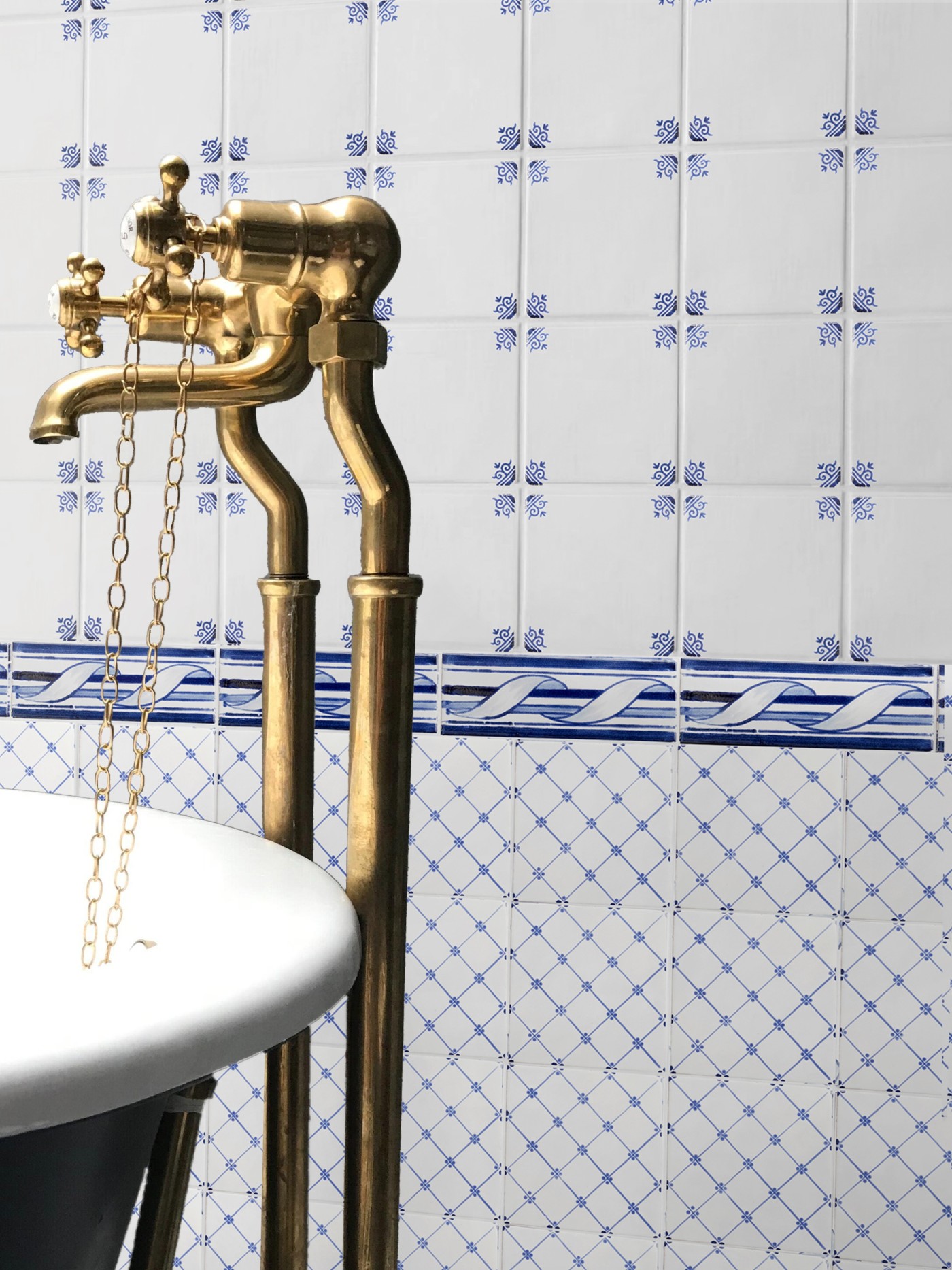 a bathroom with a brass faucet and blue and white patterned tiles.