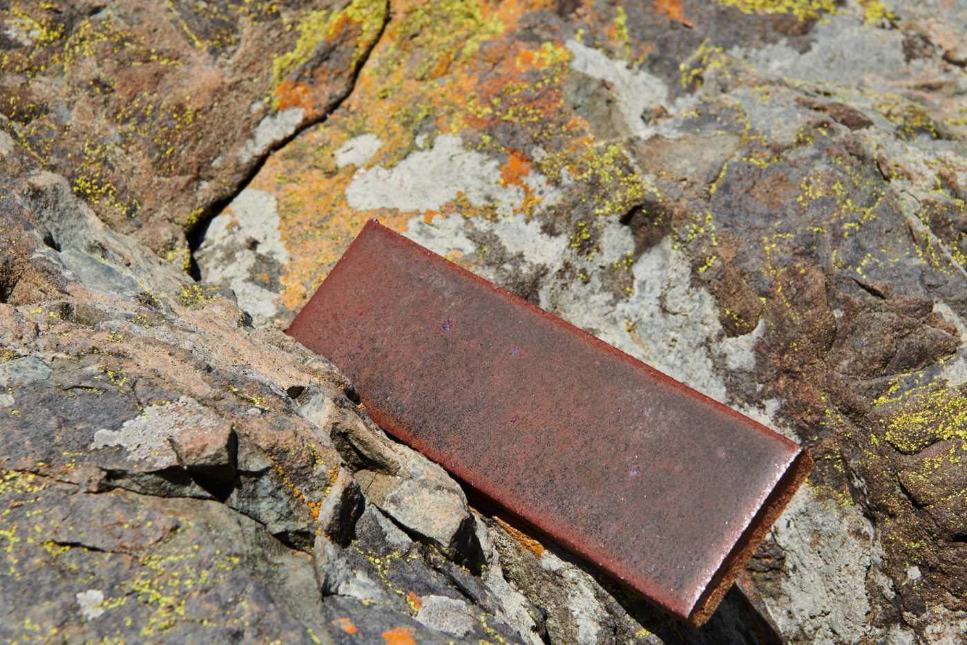 a metallic brown rectangular tile sitting on top of a rock.