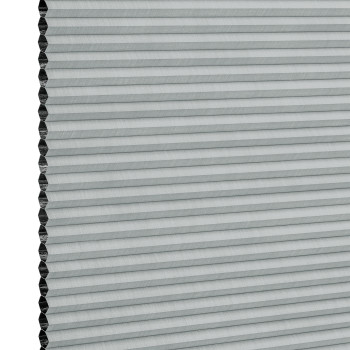 Light-gray honeycomb (cellular) blind, mounted vertically with narrow horizontal pleats and exposed hexagonal cells at the left edge; fully closed, filtering light; close-up view against a white background.