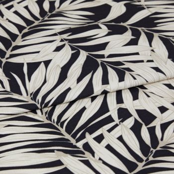 A folded decorative fabric with cream palm-leaf print on a black background; the layers overlap, emphasizing texture and weave, shown in a close-up under soft, even lighting.