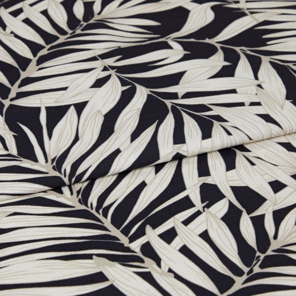A folded decorative fabric with cream palm-leaf print on a black background; the layers overlap, emphasizing texture and weave, shown in a close-up under soft, even lighting.