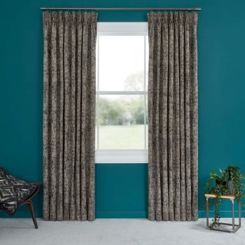 Full-length pleated gray textured curtains, on a metal rod and pulled aside, framing a white window; teal-painted wall, carpeted floor, chair left and potted plant on table right, daylight outside.