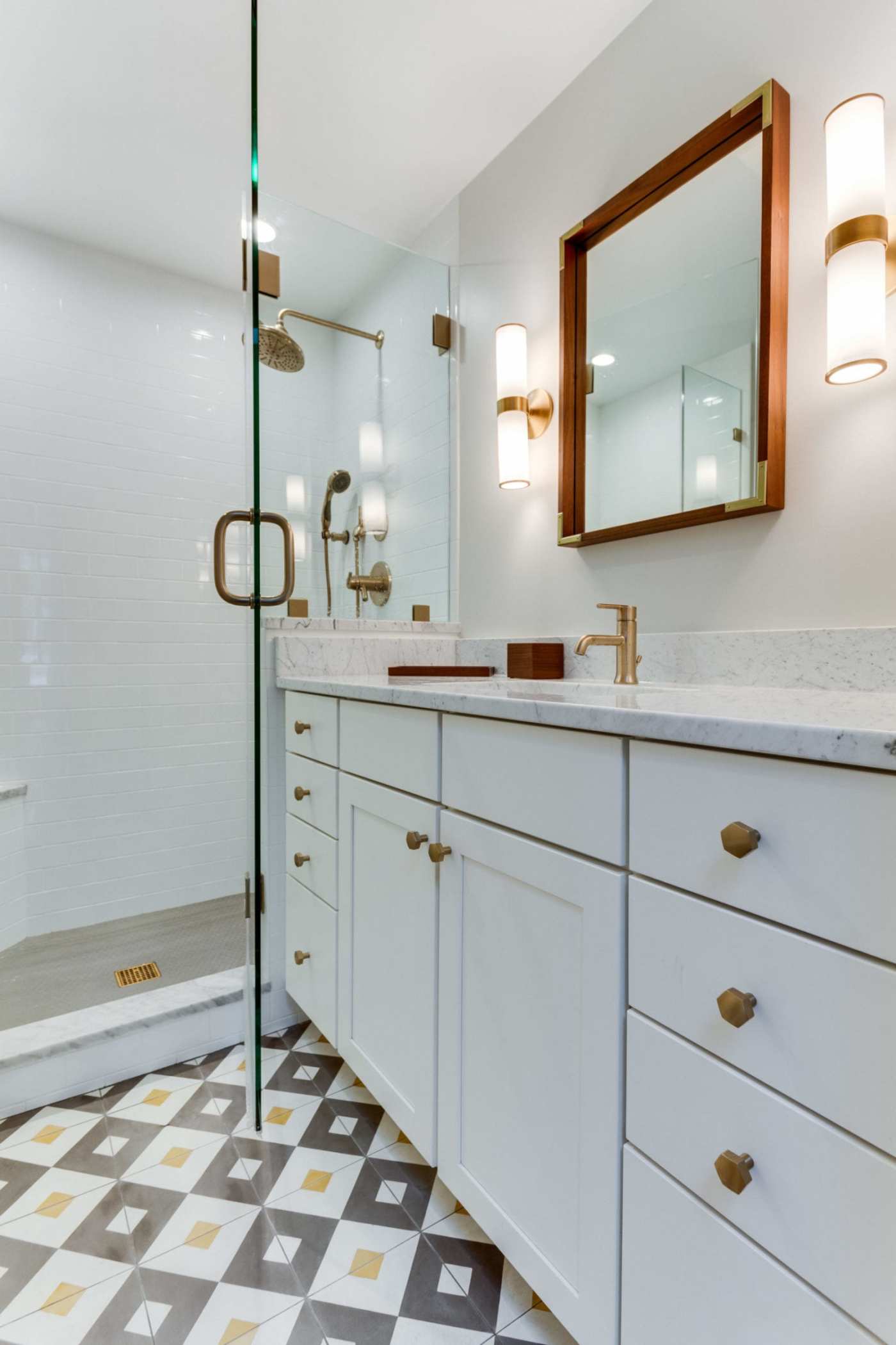 a bathroom with a white, black, and yellow tile floor and a glass shower.