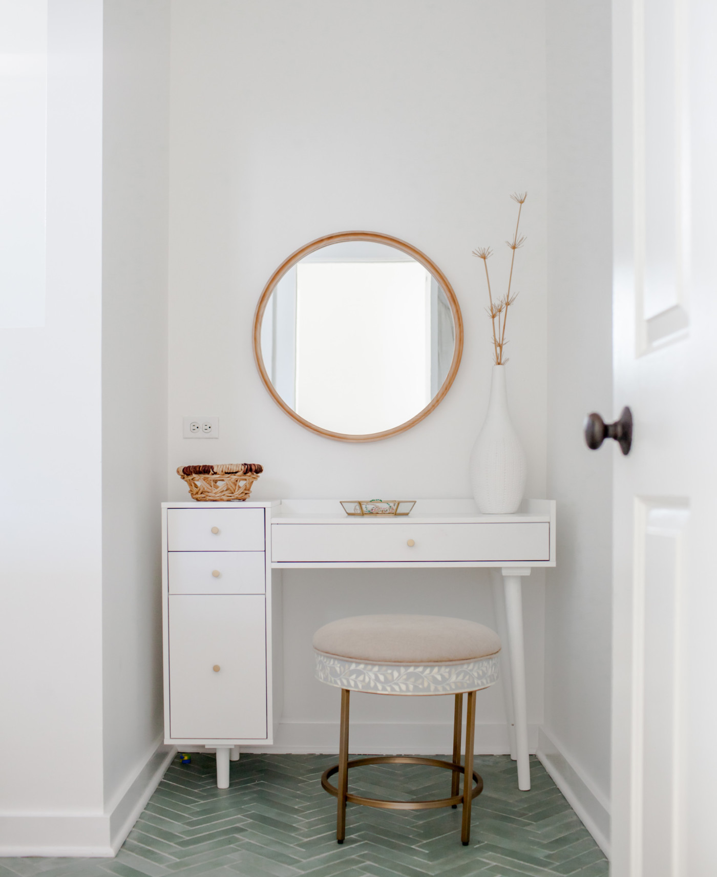 a white vanity with a round mirror and green tiled floor.