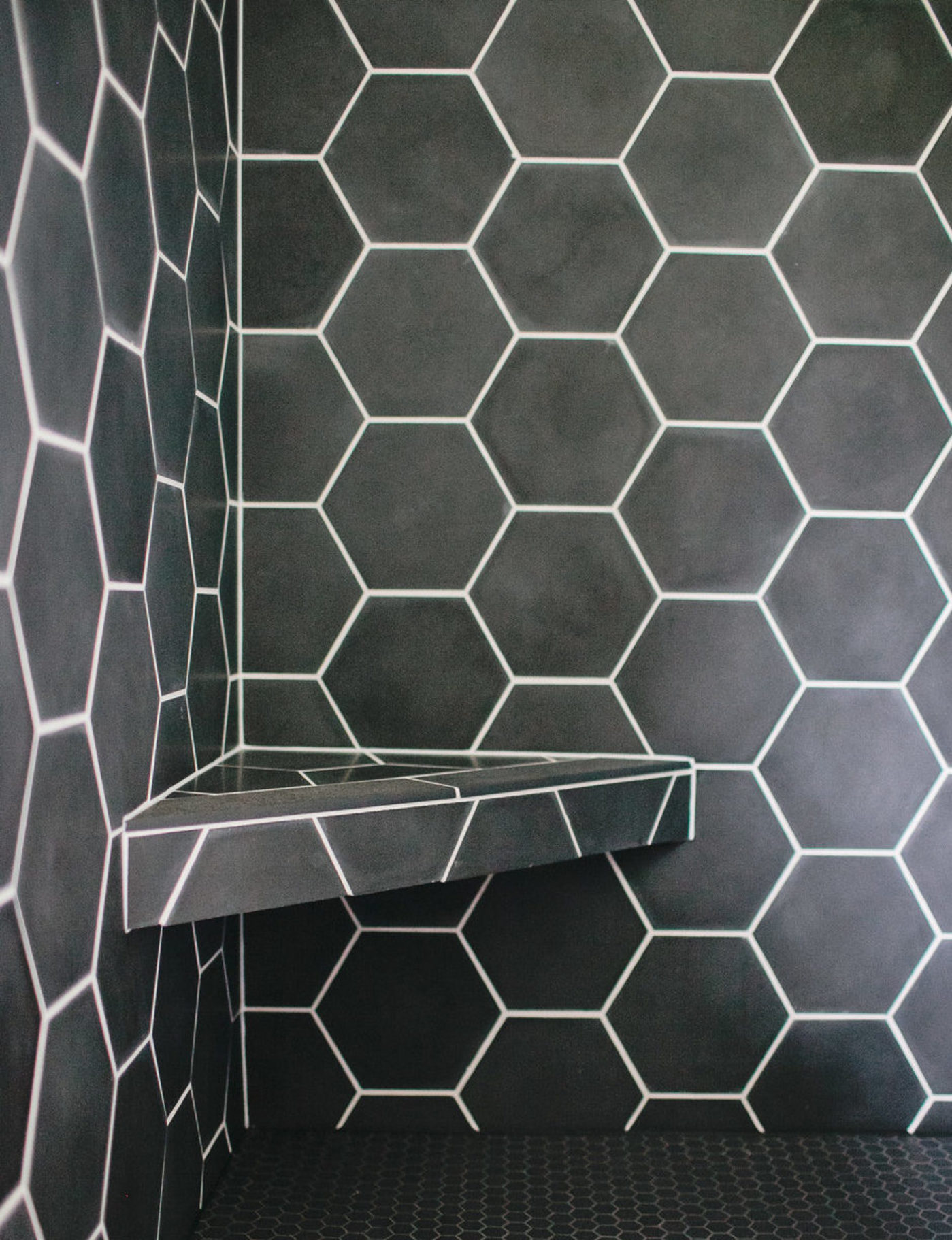 a black hexagon tiled shower with a shelf.