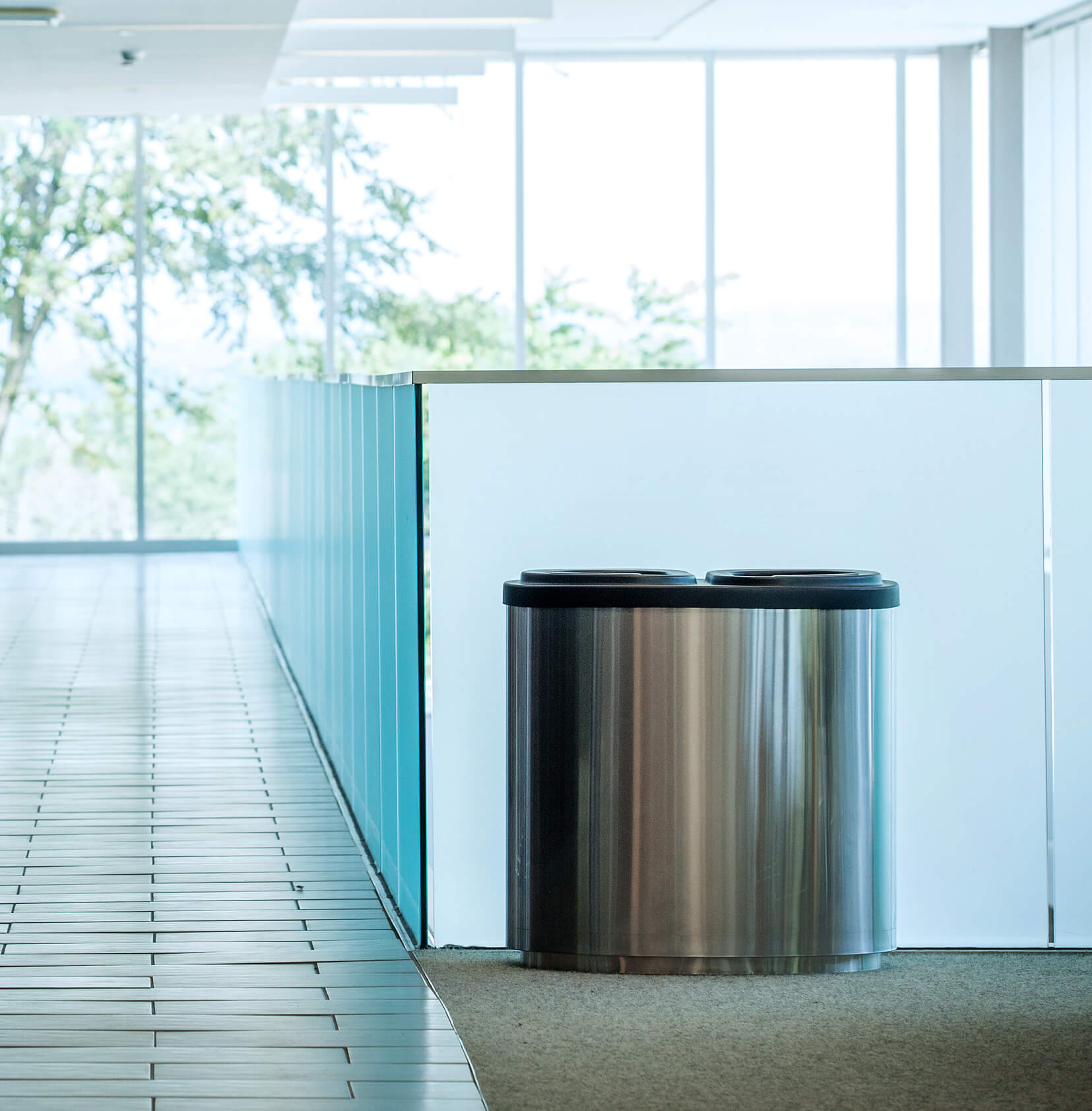 double recycling and waste bin sitting against a glass wall in a modern corporate office