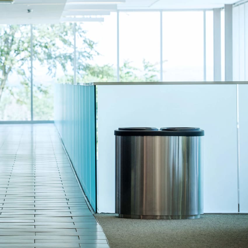 double recycling and waste bin sitting against a glass wall in a modern corporate office