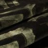 Velvet-like patterned fabric with dark olive and black abstract geometric print; folded into overlapping layers, showing soft nap and woven texture in dim, close-up studio lighting.