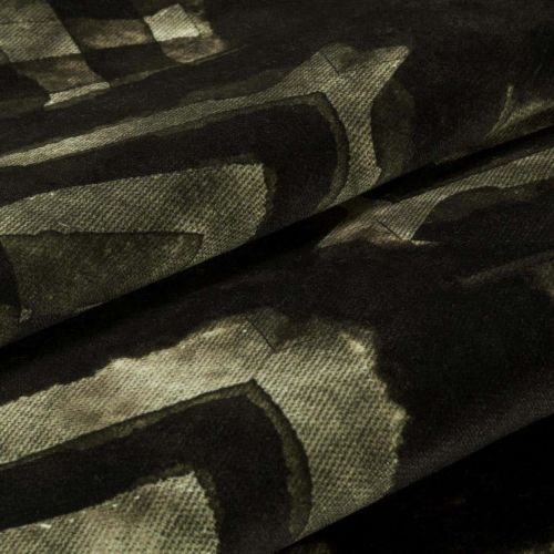 Velvet-like patterned fabric with dark olive and black abstract geometric print; folded into overlapping layers, showing soft nap and woven texture in dim, close-up studio lighting.