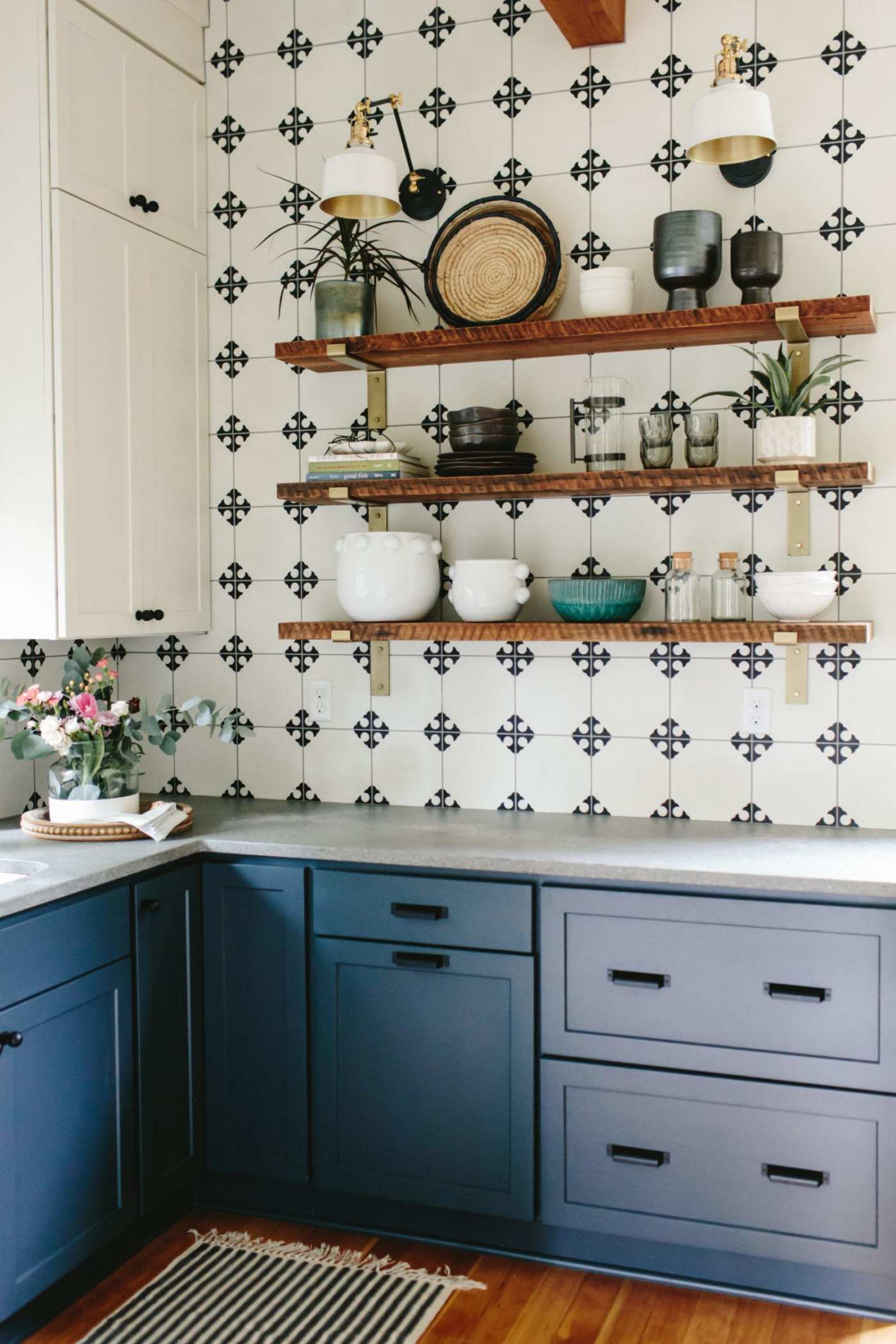 a blue and white kitchen with wooden shelves and a black and white tiled wall.