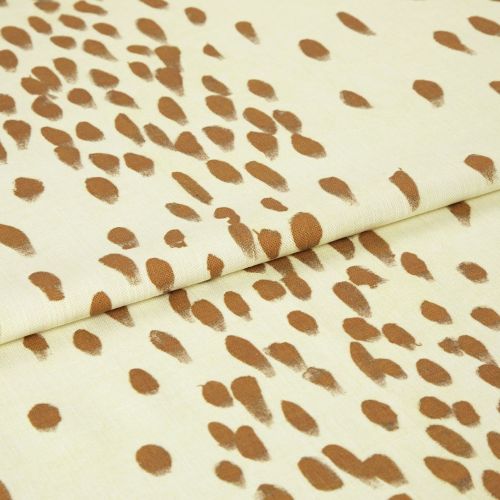 Cream woven fabric patterned with irregular brown brushstroke teardrop spots (object), folded once with a visible seam (action), close-up studio shot with even lighting showing texture (context).