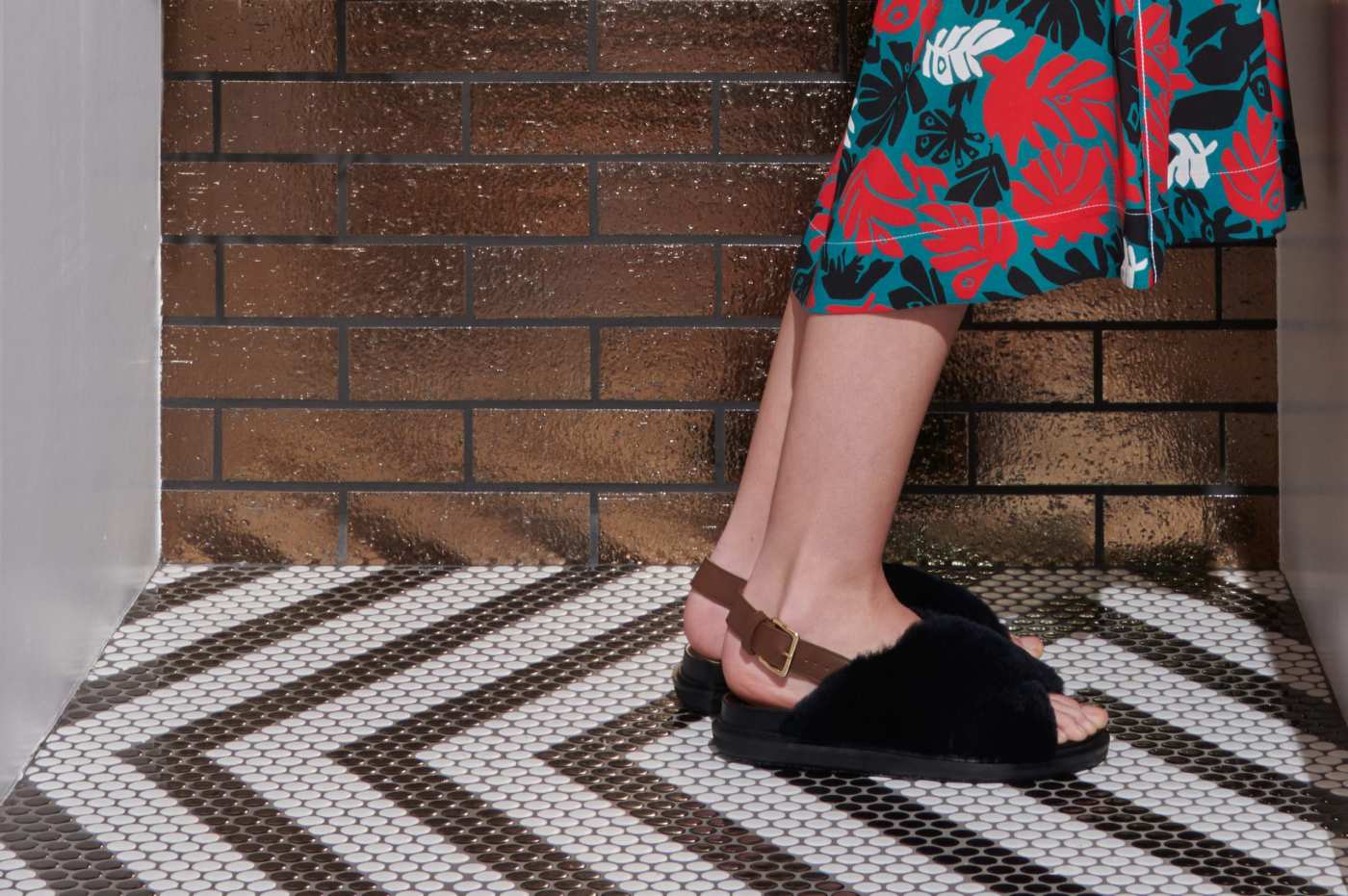 a woman standing on a tiled floor in a floral dress and sandals.