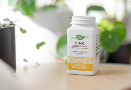 A bottle of Zinc Lozenges sitting on a wooden table with plants in the background.