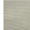 Beige honeycomb (cellular) blind with horizontal pleats and visible hexagonal cell ends at left, fully lowered and closed, blocking light; close-up filling the frame against a neutral, studio-lit background.