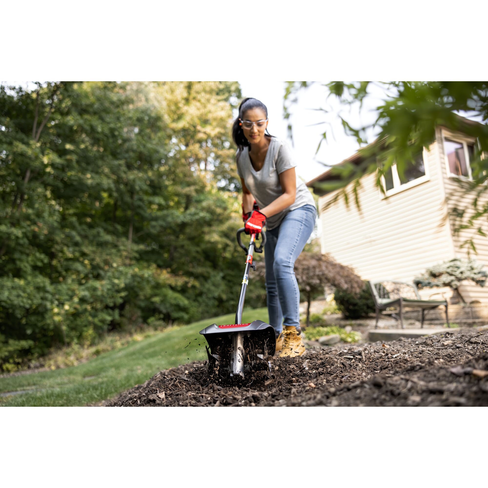 CRAFTSMAN cultivator attachment head in front view tending to mulch in backyard in gray shirt and jeans
