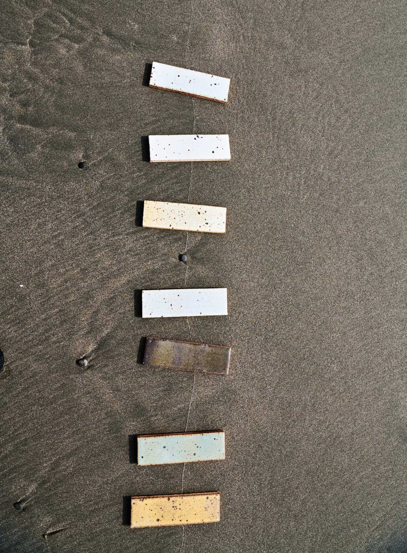 a set of multicolored rectangle tiles spread along the sand at the beach.