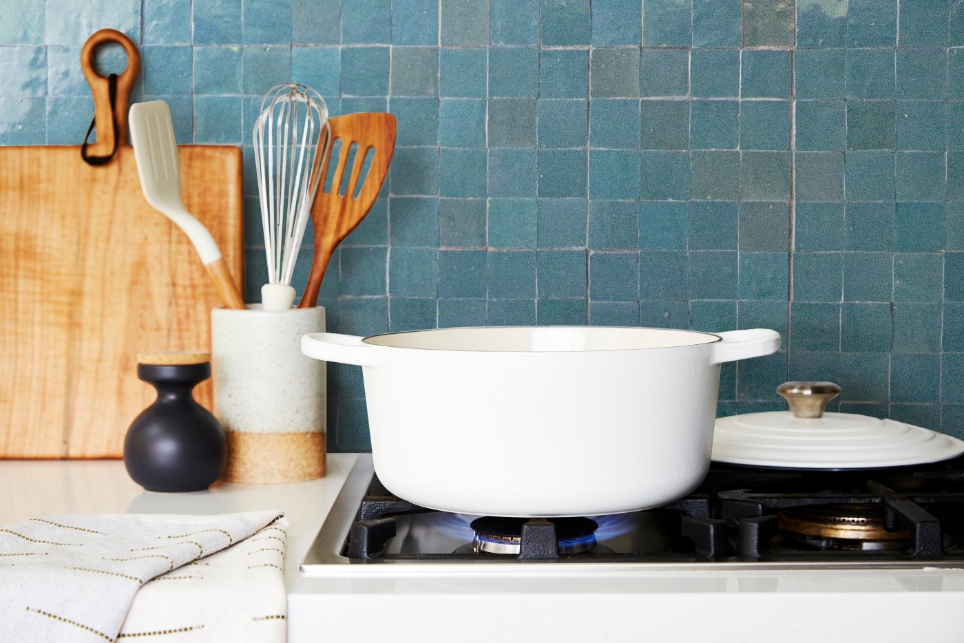 a white pot on top of a stove in front of a green tile backsplash