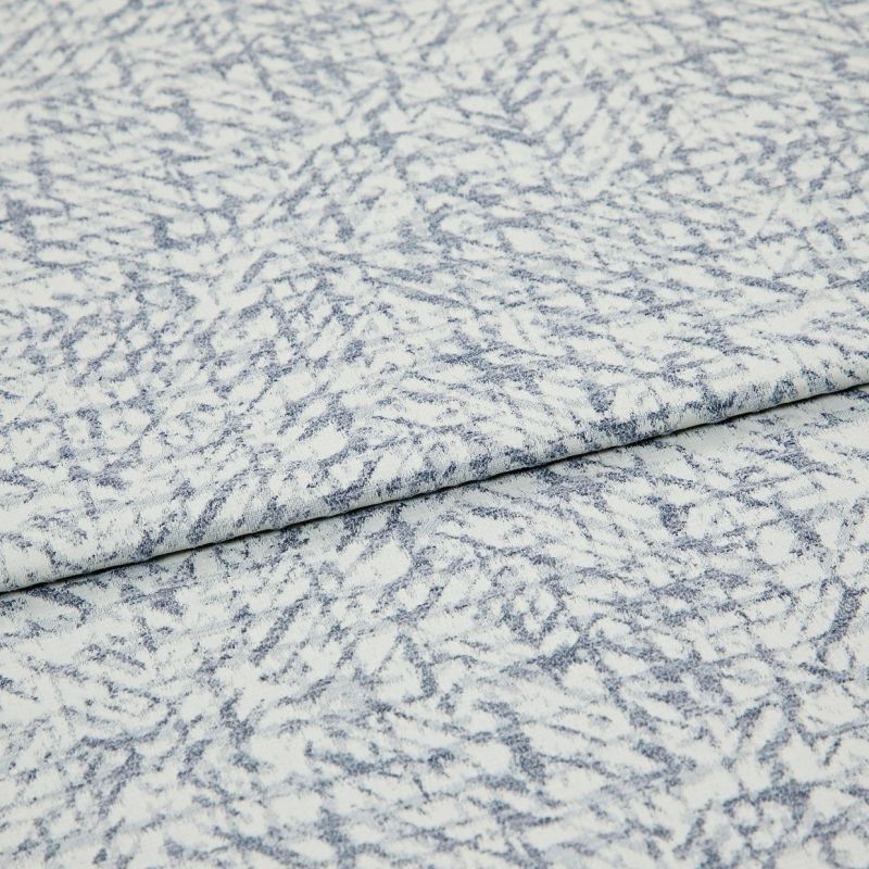 Light blue-and-white patterned fabric folded once, overlapping; textured woven surface with irregular, fern-like striations, photographed close-up under even studio lighting.