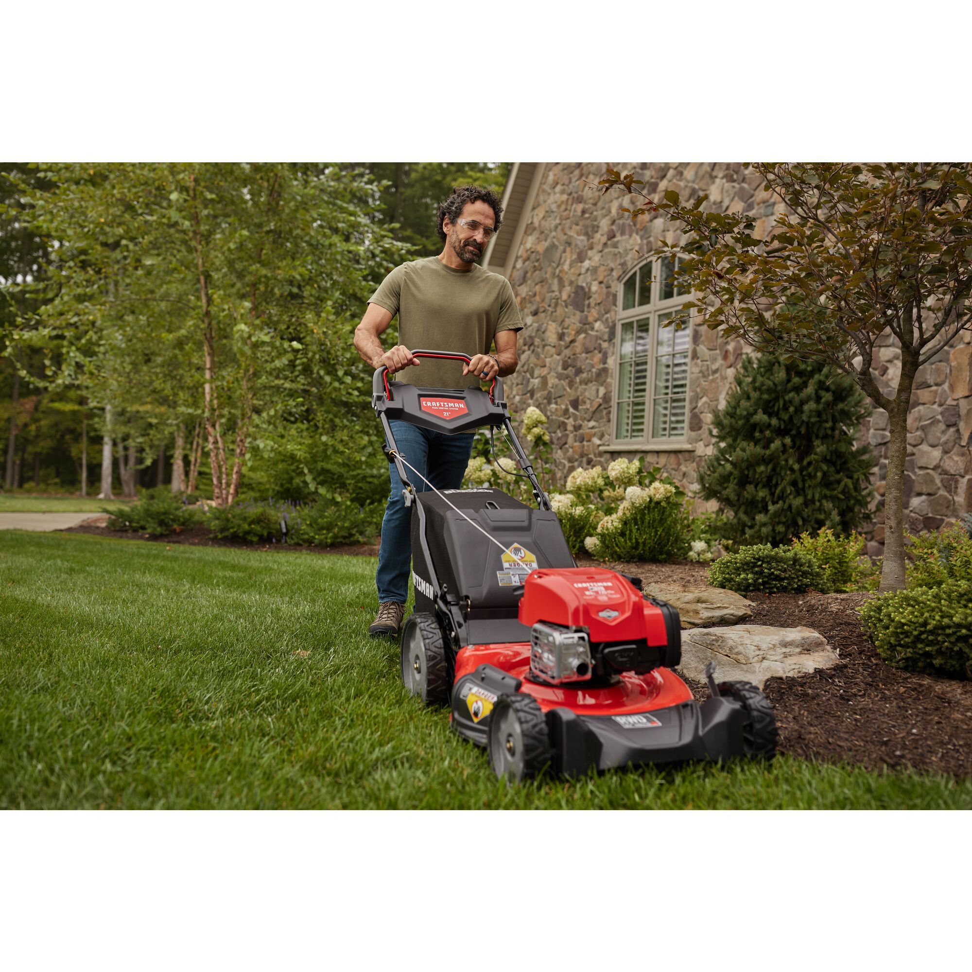 CRAFTSMAN M320 RWD Self-Propelled Mower mowing a well-groomed lawn in front view in green shirt and jeans