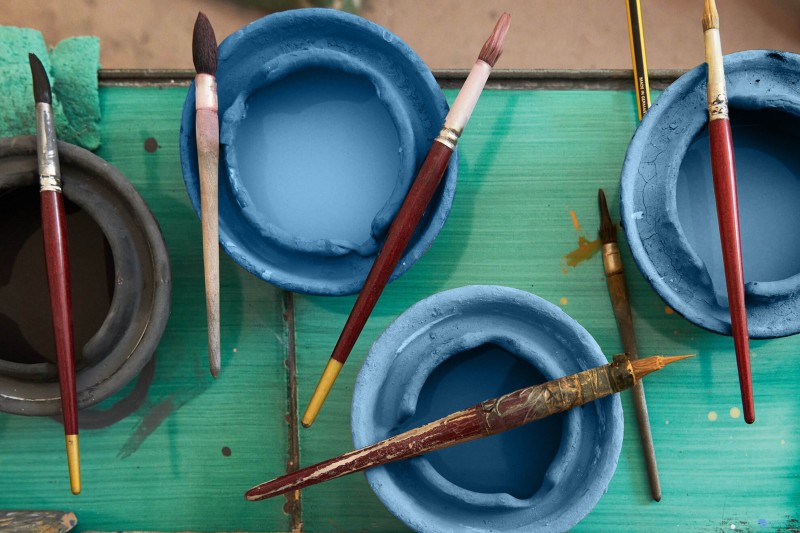 a group of paint brushes and bowls on a green table.