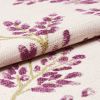 Cream woven fabric with purple floral embroidery; folded to reveal raised tufted stitching; close-up macro view on a neutral surface with soft, even lighting.