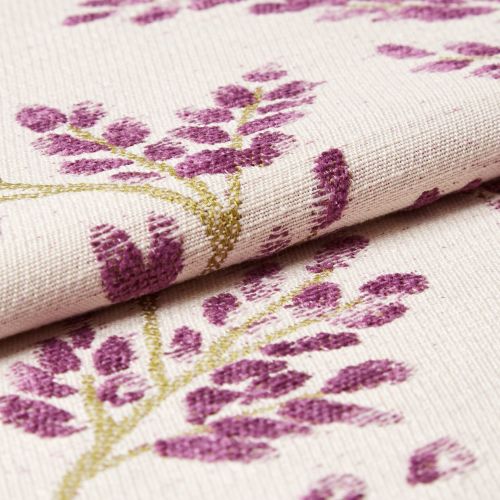 Cream woven fabric with purple floral embroidery; folded to reveal raised tufted stitching; close-up macro view on a neutral surface with soft, even lighting.