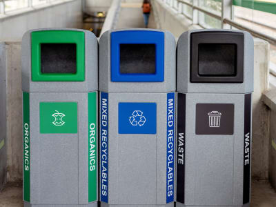 triple waste recycling and organics bins with color coded openings and labels shown in a municipal transit station