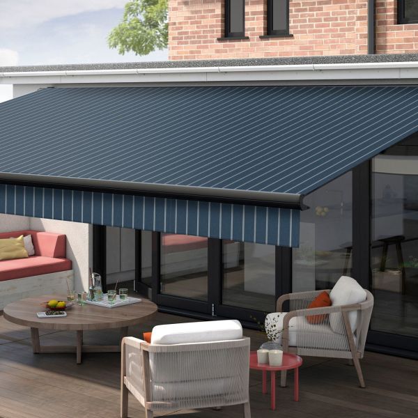 Blue striped retractable awning with matching valance extended over patio glass doors, shading a furnished terrace—wooden coffee table, cushioned chairs and bench—attached to a brick-faced modern house under daylight.