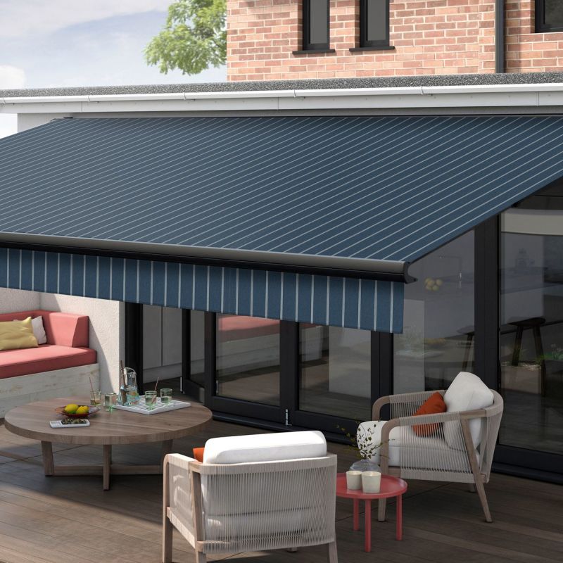 Blue striped retractable awning with matching valance extended over patio glass doors, shading a furnished terraceâ€”wooden coffee table, cushioned chairs and benchâ€”attached to a brick-faced modern house under daylight.