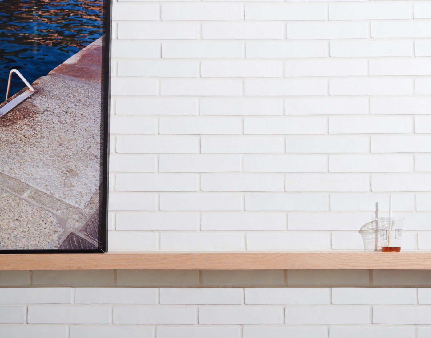 a wooden shelf on a white brick wall with a picture of a pool on it.