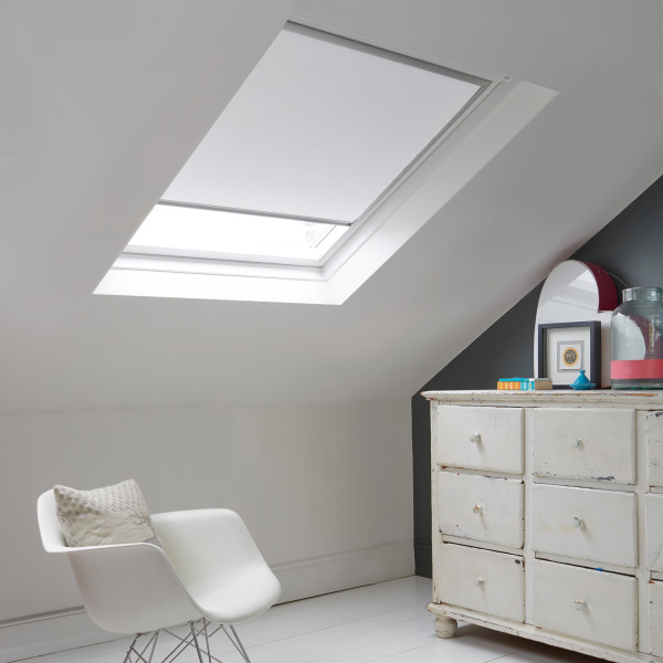 Room with white eaves wall, dark blue-grey wall to right with a shabby chic white drawer unit, a contemporary white chair, white painted floorboards and a skylight blind in white.