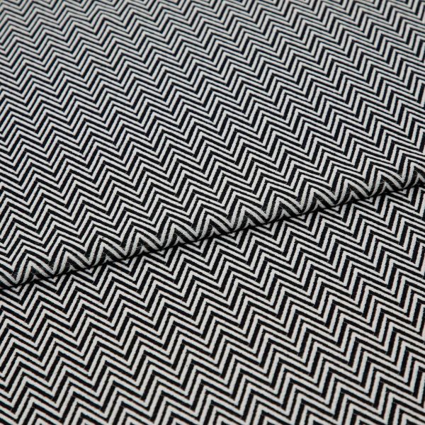 Black-and-white chevron-patterned fabric, folded across the center and showing dense, repeating zigzag lines; lying flat, closely cropped, with even studio lighting highlighting its texture.