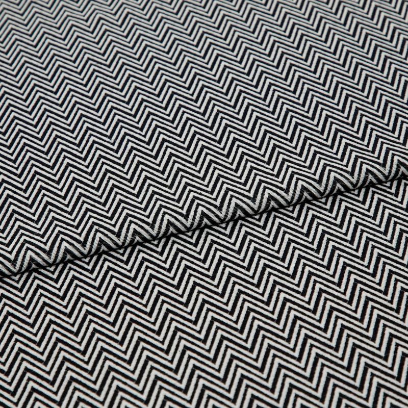 Black-and-white chevron-patterned fabric, folded across the center and showing dense, repeating zigzag lines; lying flat, closely cropped, with even studio lighting highlighting its texture.