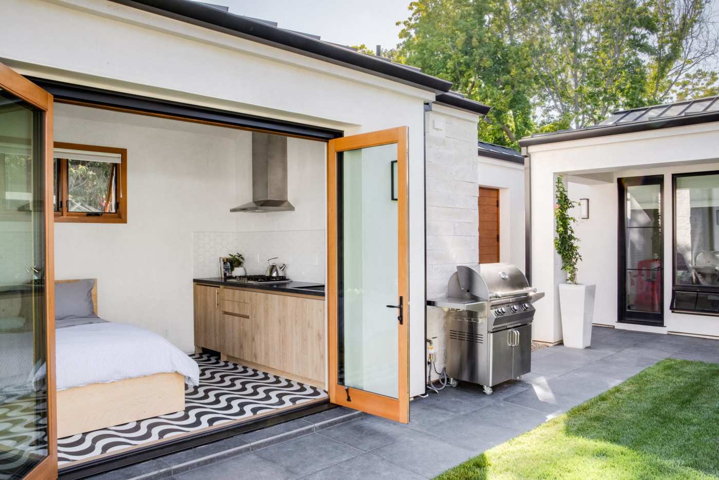 an open bedroom leading to a backyard with a barbecue and a lawn.