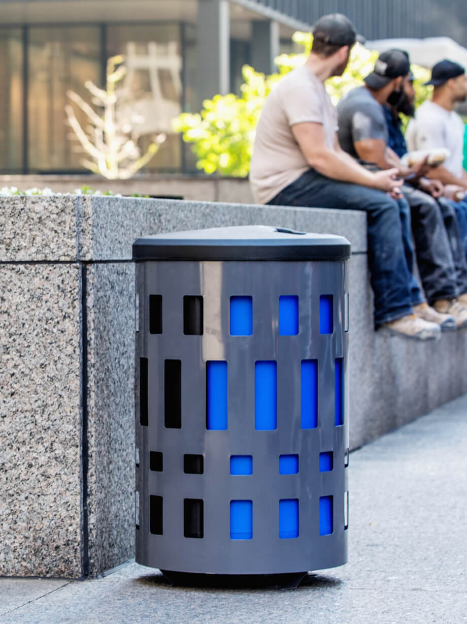 metal outdoor durable waste container with a plastic canopy lid and large capacity liners beside a bench in a city park