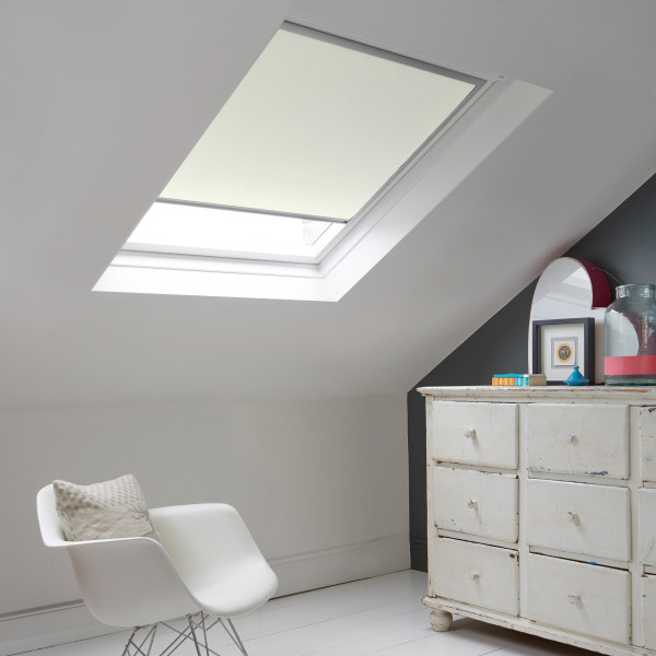 Room with white eaves wall, dark blue-grey wall to right with a shabby chic white drawer unit, a contemporary white chair, white painted floorboards and a skylight blind in pale beige.