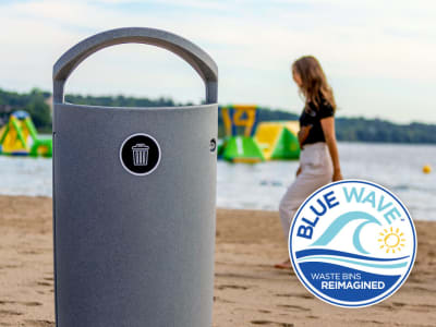 grey waste bin at the beach with woman walking by along waterfront