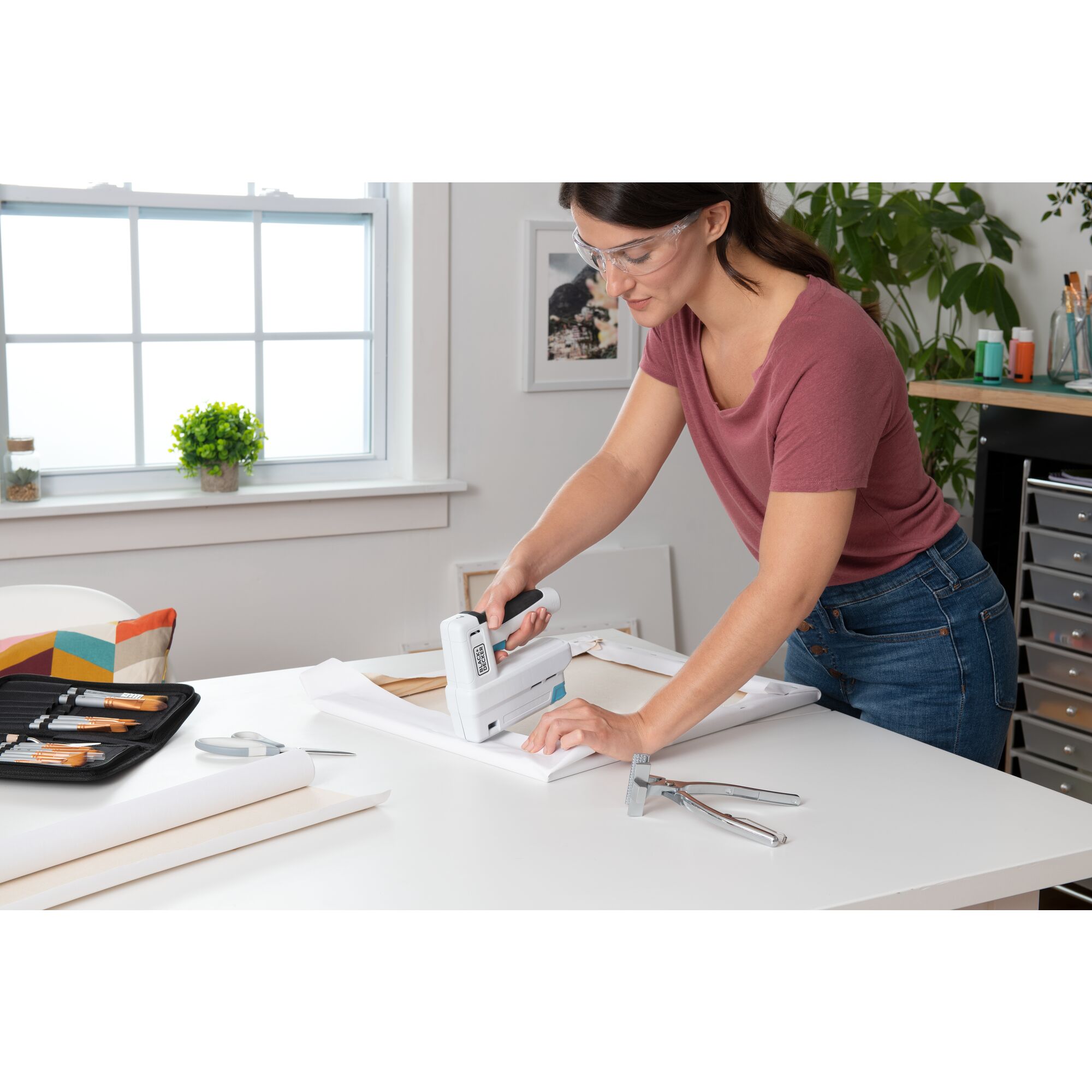 woman in craft room using a BLACK+DECKER cordless powered stapler to make a canvas