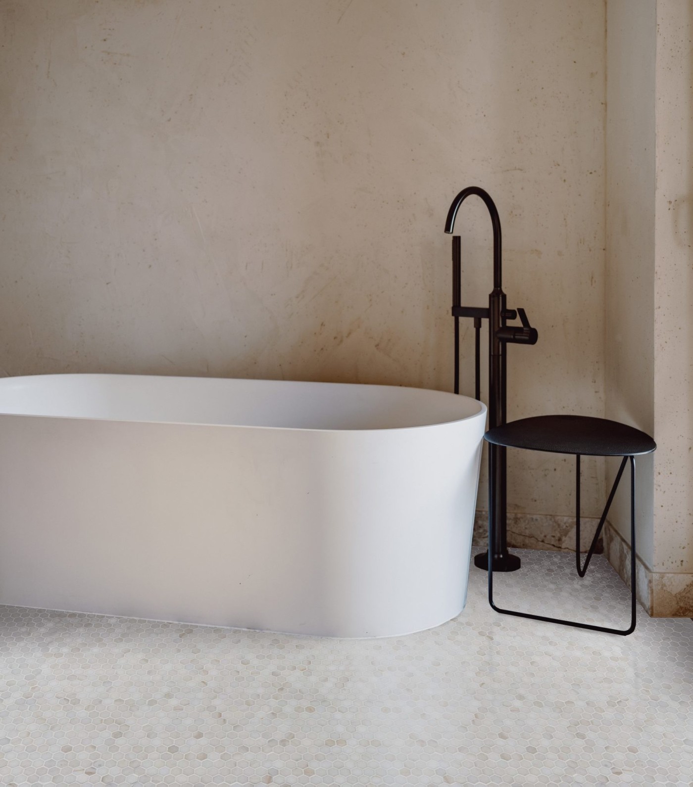 a white bathtub sits next to a stool in a bathroom.