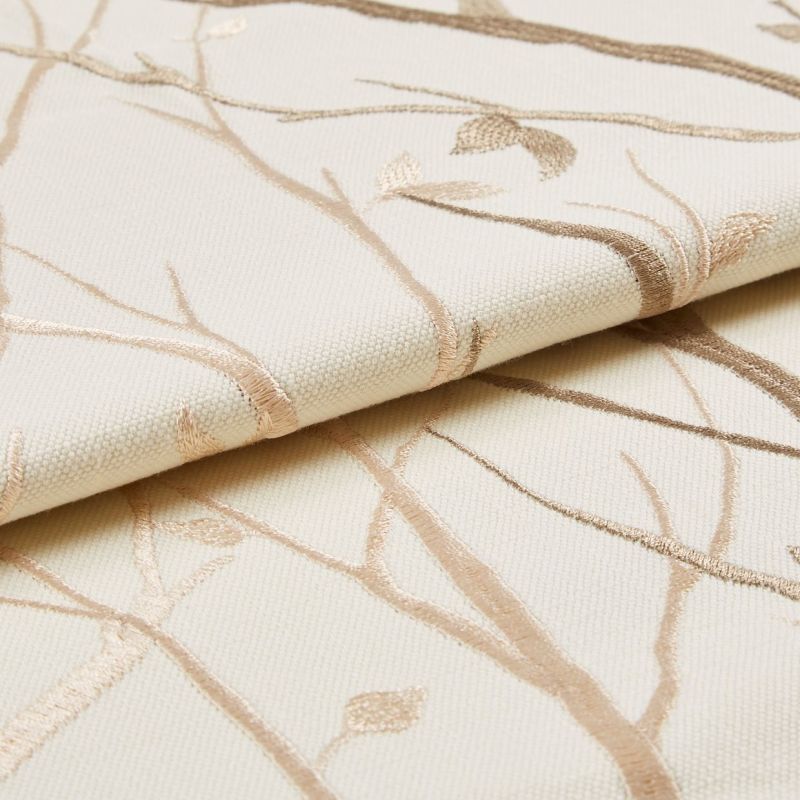 Cream woven fabric with beige embroidered branches (curtain sample), folded to show raised embroidery and textured weave; close-up studio setting with soft, neutral lighting.