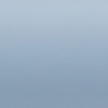 Smooth pale blue gradient surface occupying the frame; shading transitions from lighter at top to slightly darker bottom; evenly lit, featureless field resembling sky or painted wall.