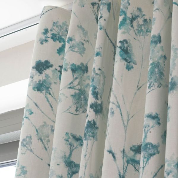 Pleated fabric drapes with a teal watercolor tree pattern, hanging closed over a window; filtering soft daylight into an interior space beneath a white cornice.