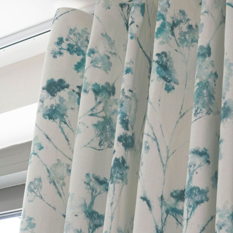 Pleated fabric drapes with a teal watercolor tree pattern, hanging closed over a window; filtering soft daylight into an interior space beneath a white cornice.
