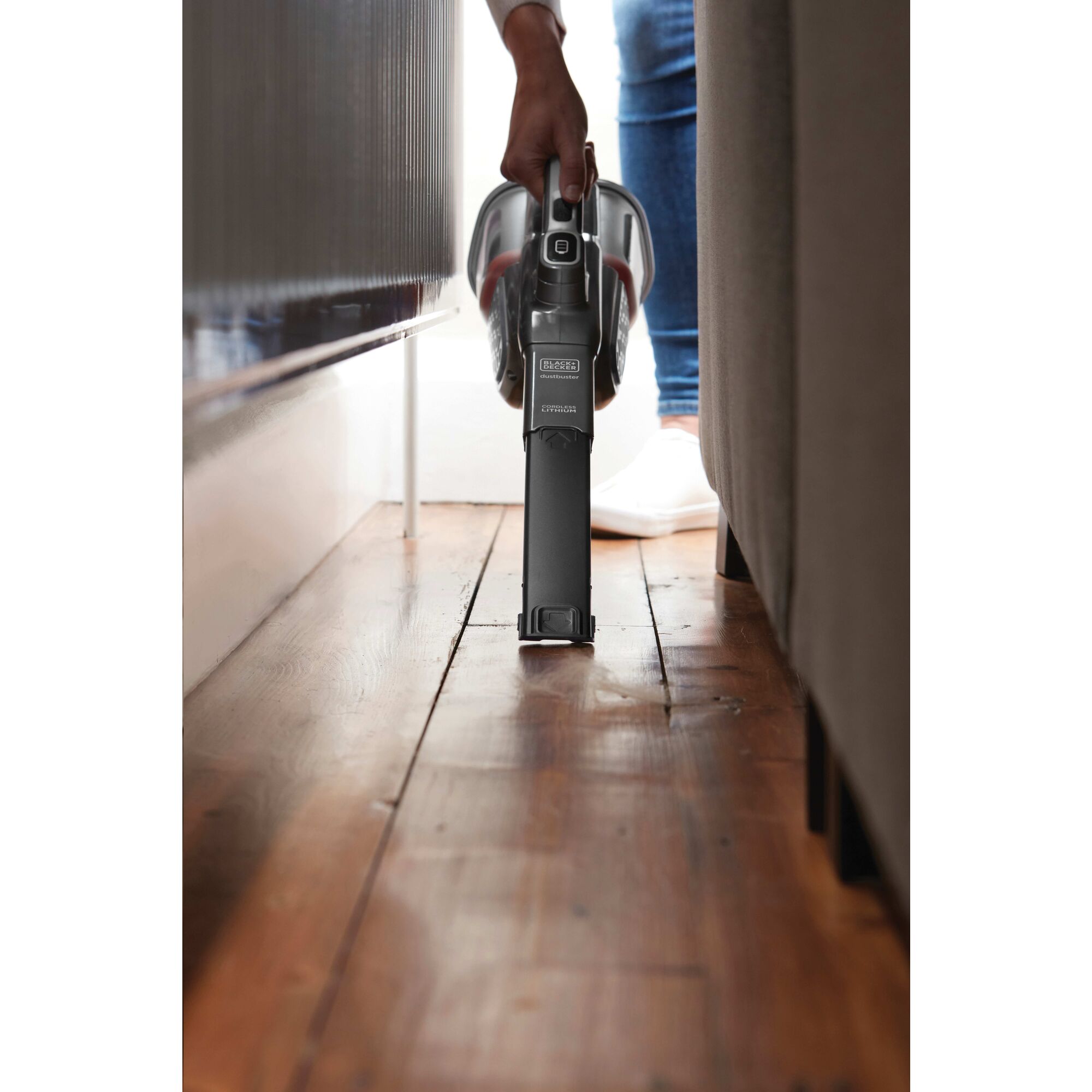 12 Volt MAX Dust buster Advanced Clean + Cordless Hand Vacuum with Powered Pet Head being used to clean behind the sofa.