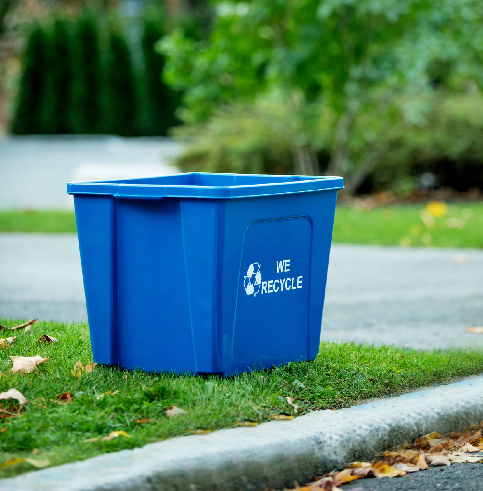 blue curbside recycling bin with we recycled stamped on the side sitting curbside along a residential street