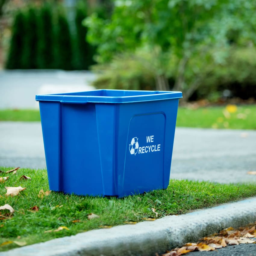 blue curbside recycling bin with we recycled stamped on the side sitting curbside along a residential street