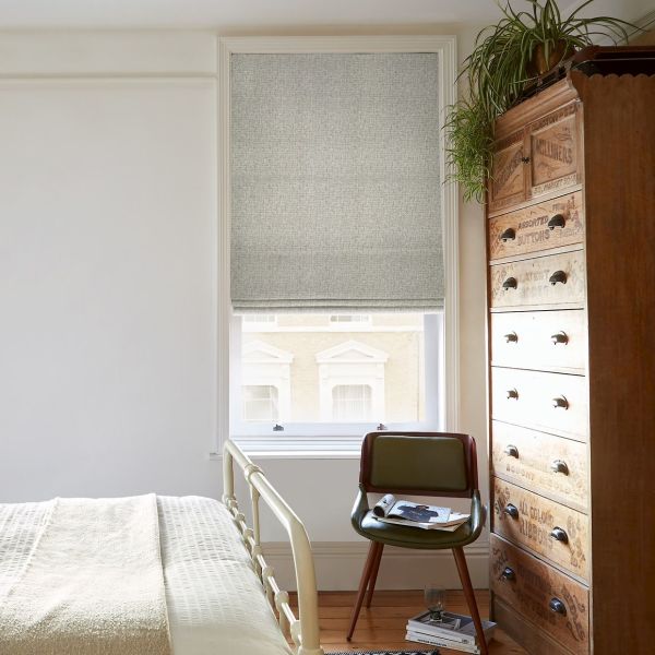 Roman fabric Roman blind, lowered, textured grey, filtering soft daylight into a cozy bedroom with a pale bed, green chair, tall vintage wooden chest, and a hanging spider plant.
ASSORTED BUTTONS; ALL COLOUR BUTTONS